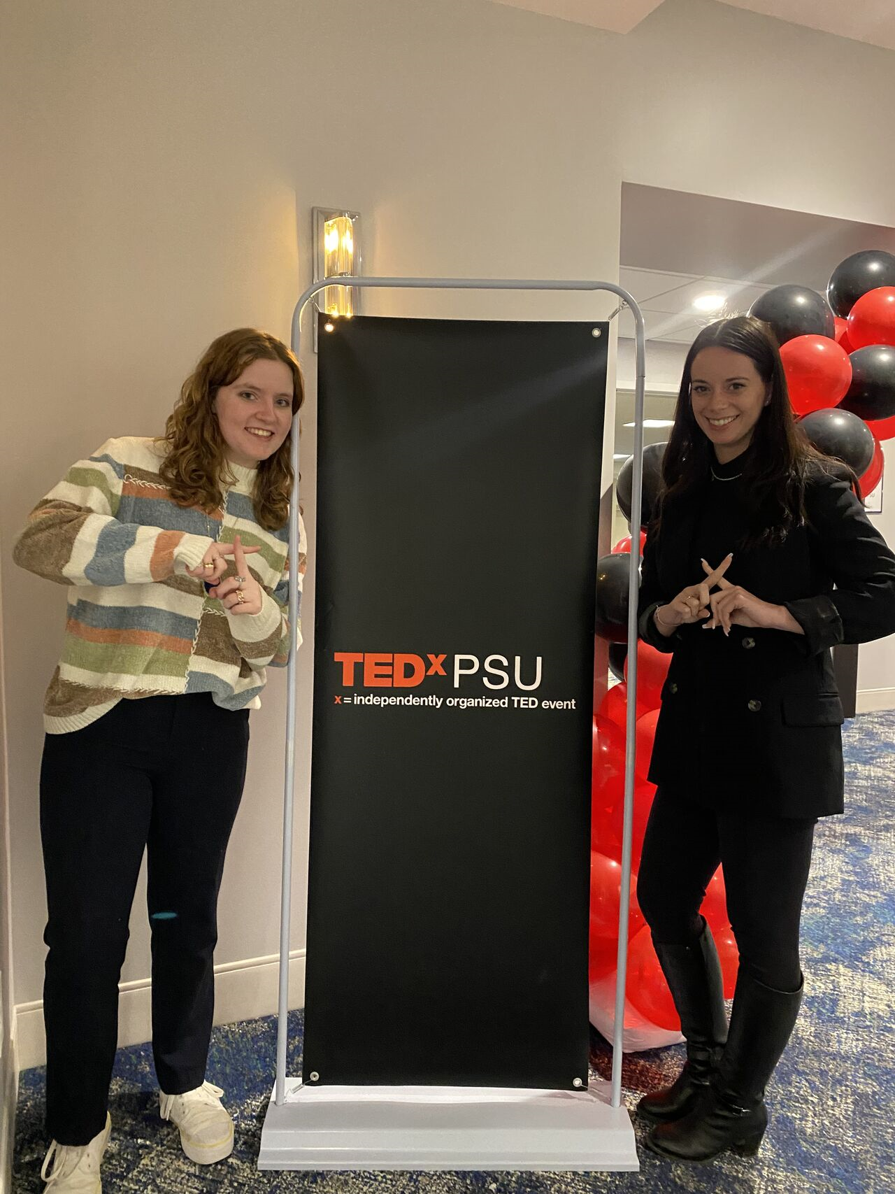 Natalie and Renee pose next to a TEDxPSU sign.