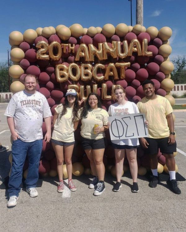 Delta Phi Members pose at a Bobcat Build Balloon Wall.