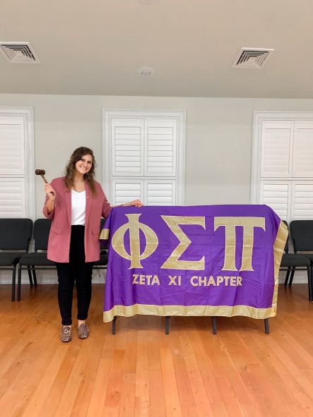 Maddie standing with a Phi Sigma Pi banner and gavel. 