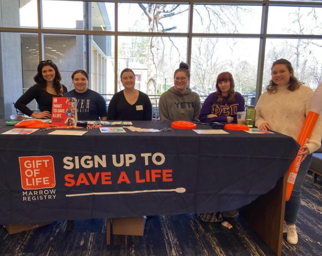 Six Members stand at the Gift of Life table and smile.