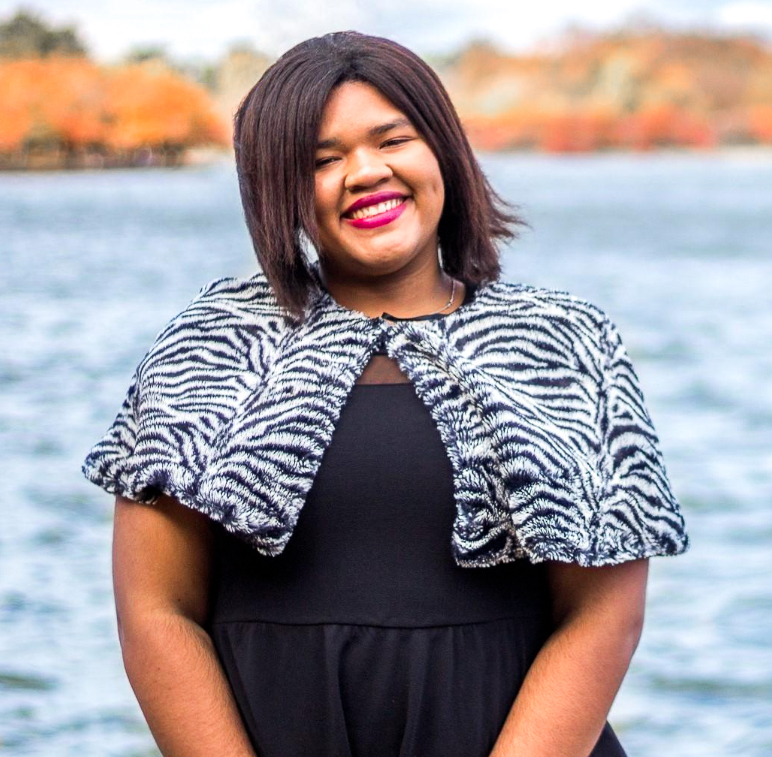 Angelica Vega smiling, wearing black formal clothing and standing in front of a lake.